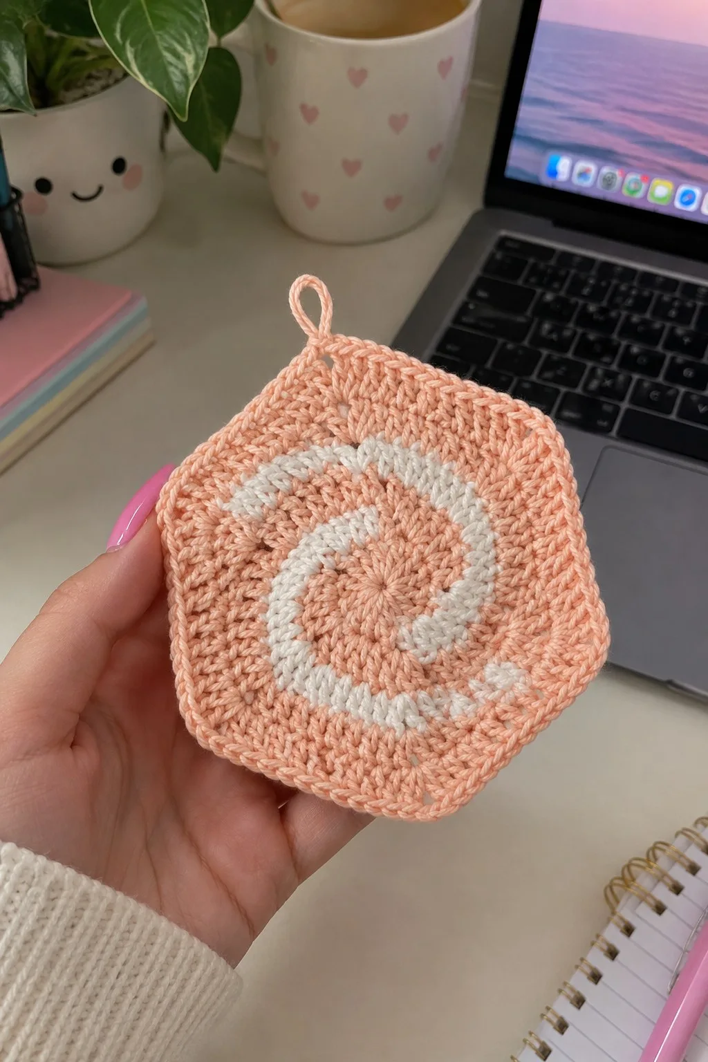 Peach cotton hexagonal potholder with white spiral surface detail and small hanging loop